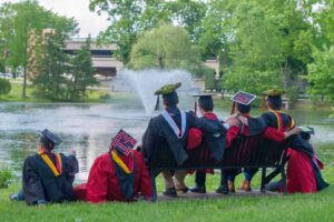 Eight graduates in regalia sitting on the banks of Passion Puddle.
